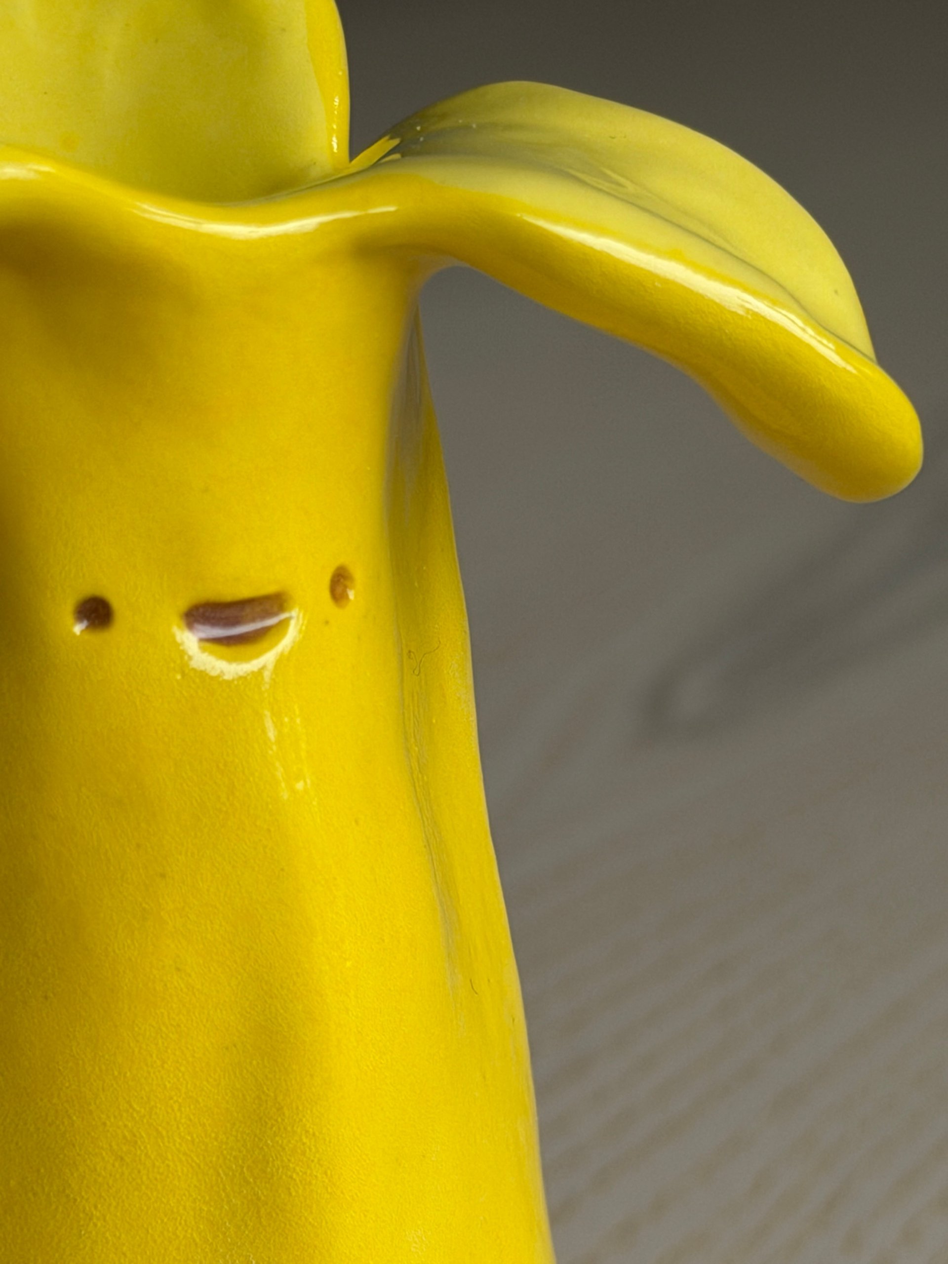 Close view of a cup's face — two small closed eyes and a little smile pressed into the clay