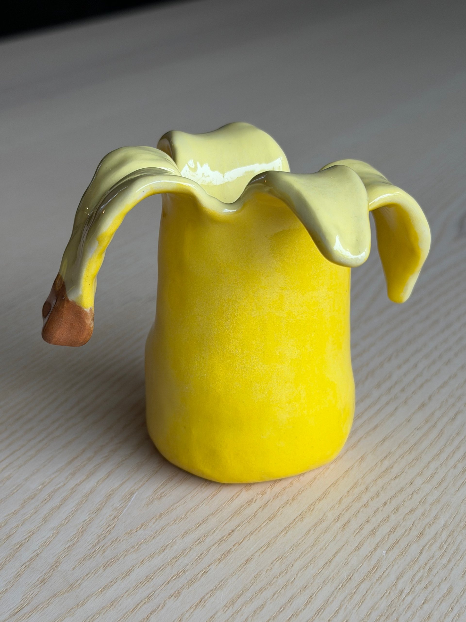 A yellow ceramic banana cup with its peel folded back over the opening and a brown stem to one side