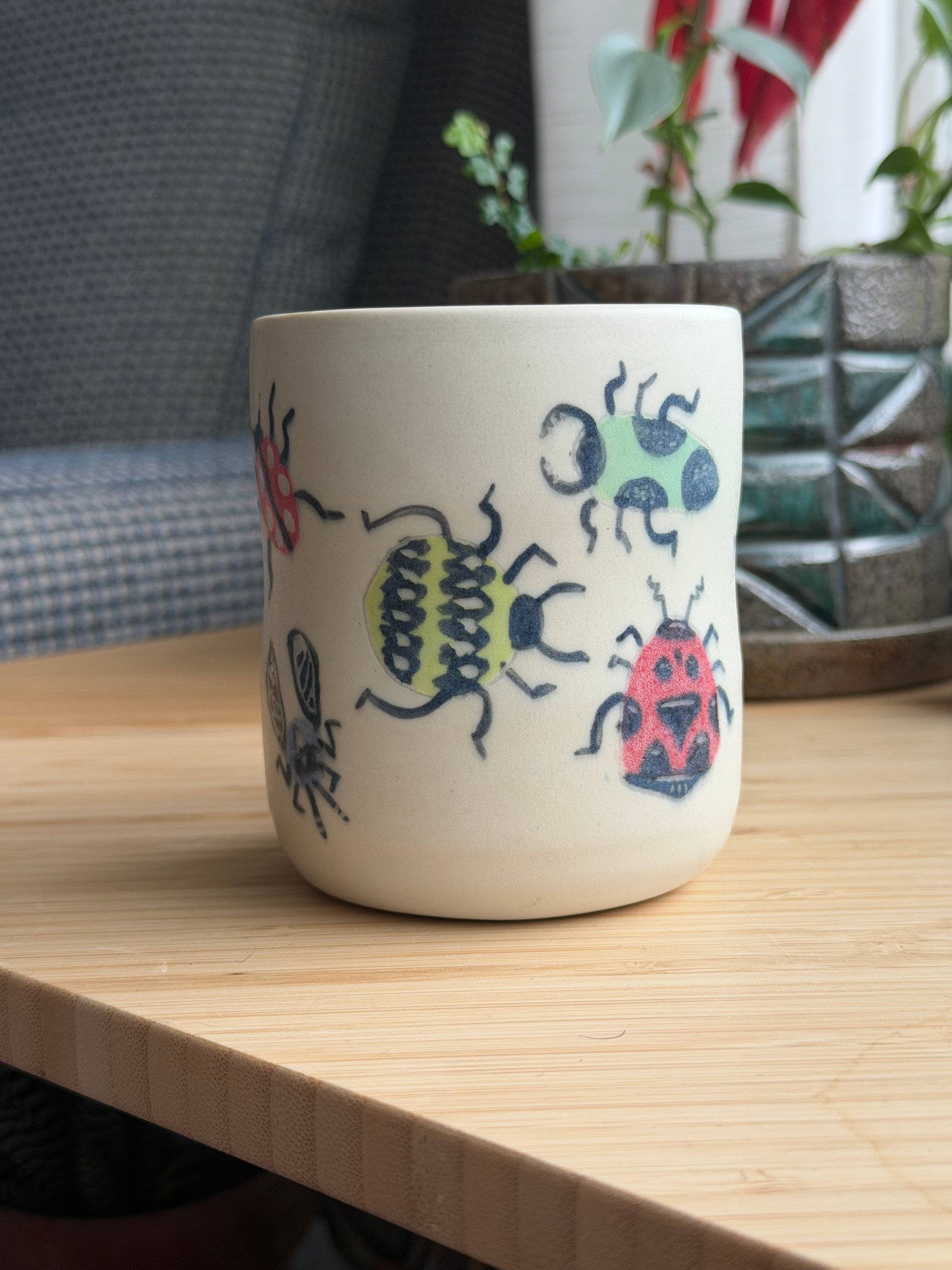 The front of the mug, a beetle, a ladybug and a green bug spread across it