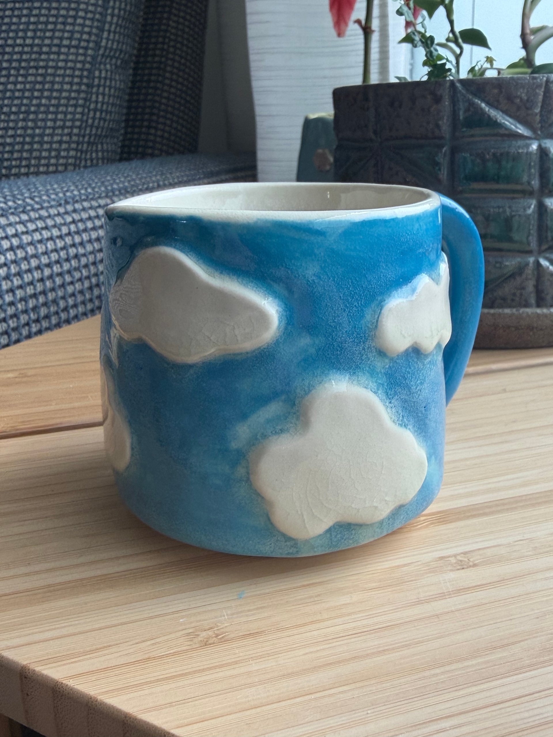 A bright blue mug with white clouds raised in relief around the outside
