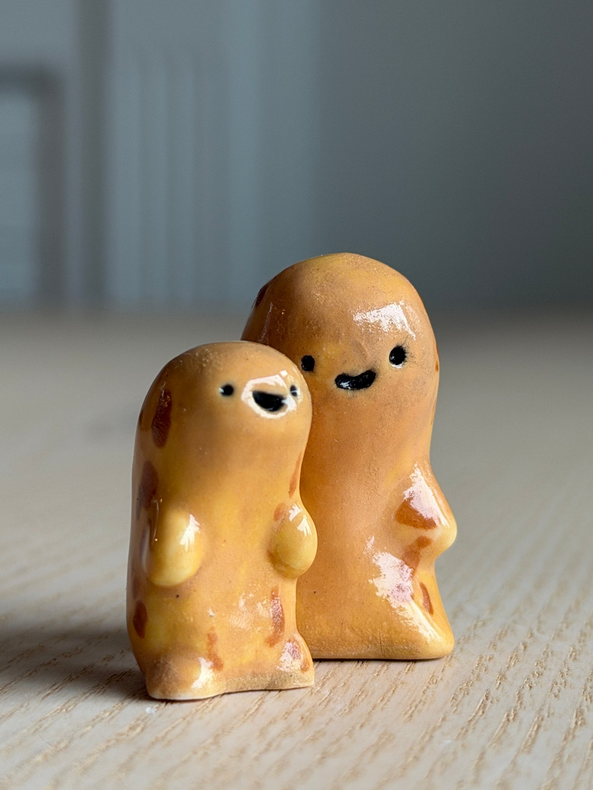 Two small tan clay beans standing side by side, each with a face and little arms
