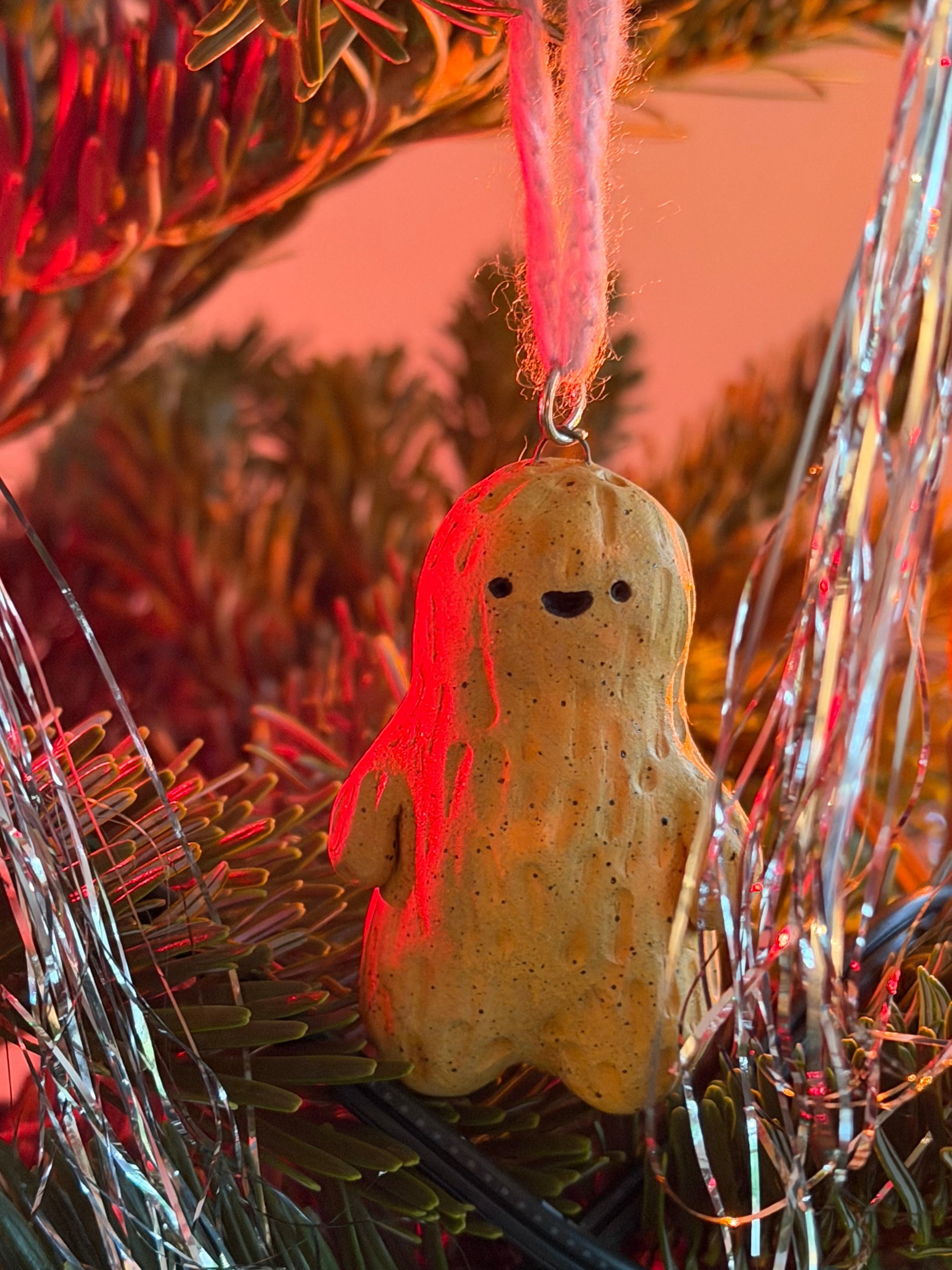 A peanut hanging among tinsel, lit warm by the tree lights