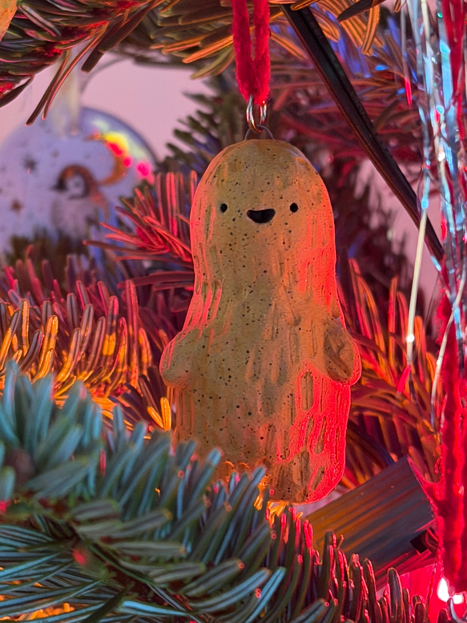 A peanut-shaped ornament with a smiling face, hanging from a ribbon on a Christmas tree