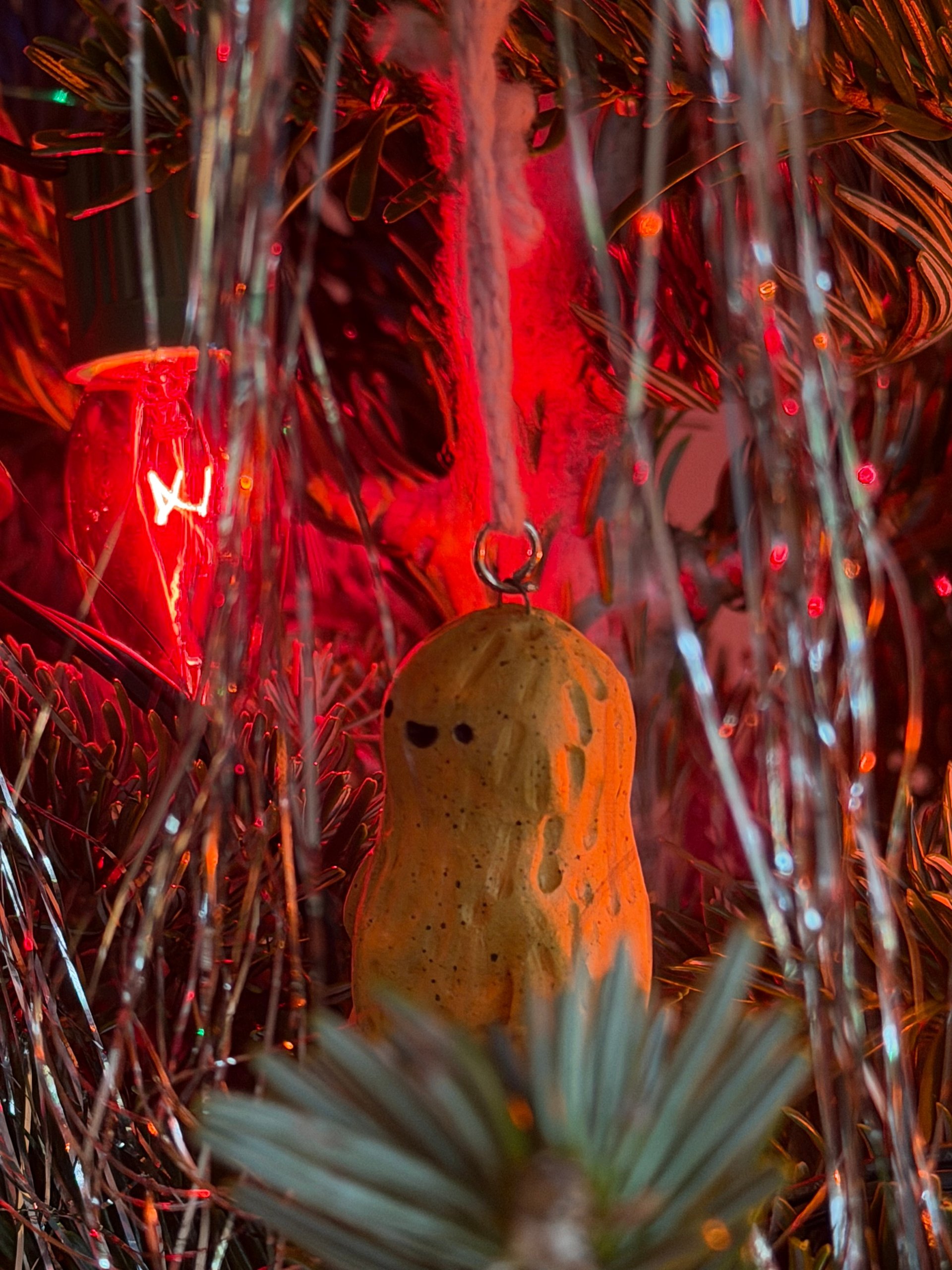 A peanut resting on a branch, tinsel and red lights behind it