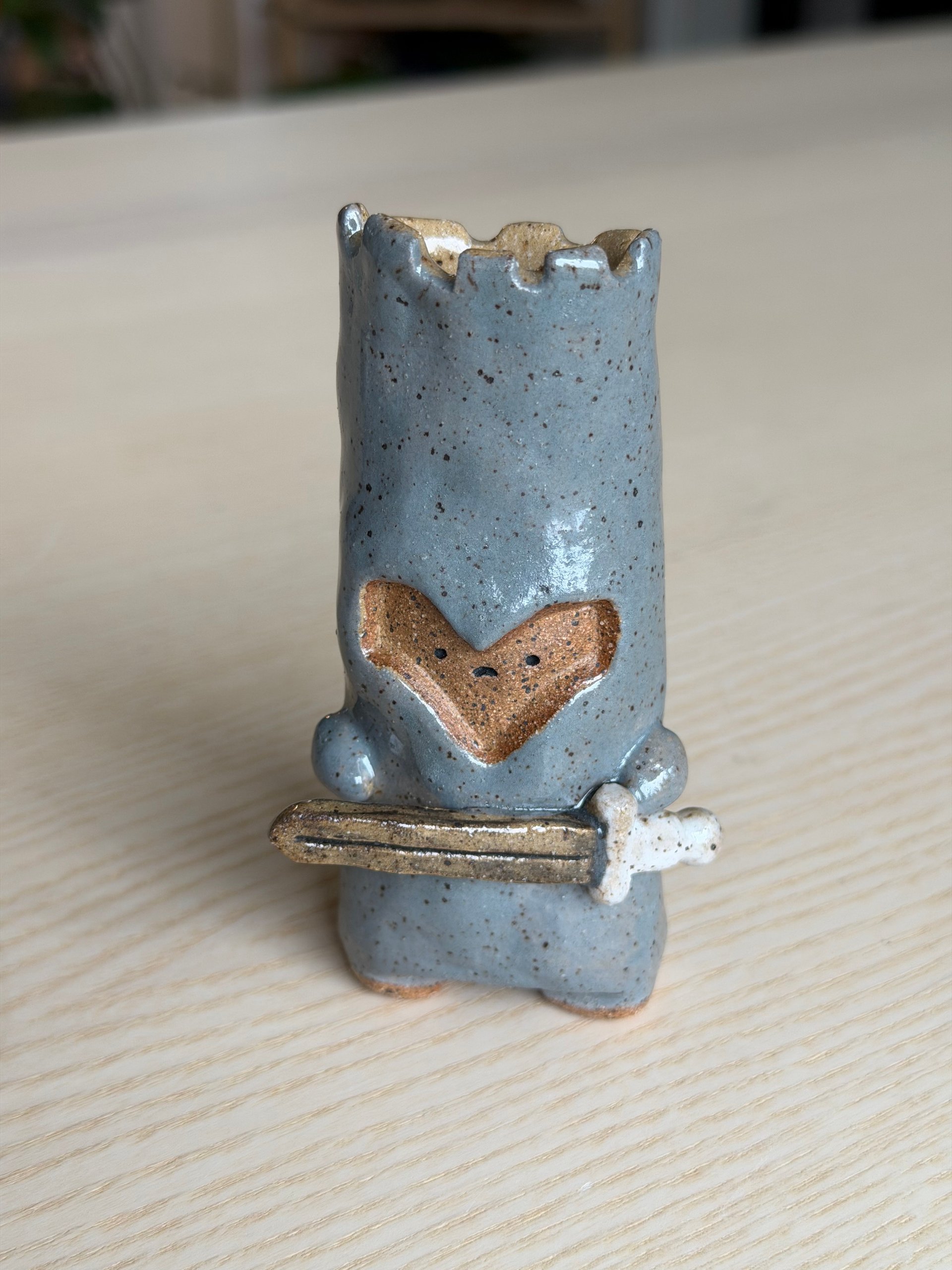 A grey speckled sprite with a battlemented top and a terracotta heart-shaped face, holding a sword