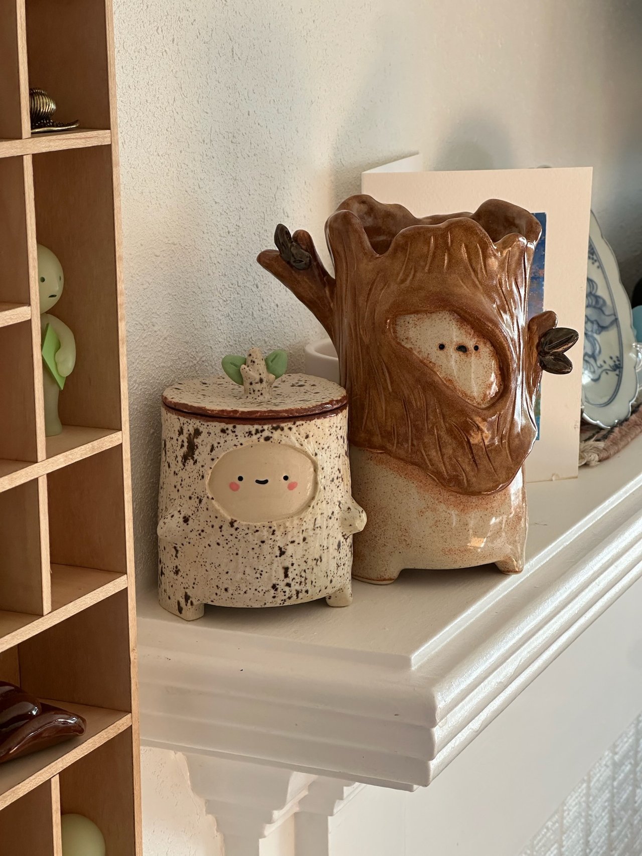 The same piece on a mantel beside a small lidded jar with a face on it
