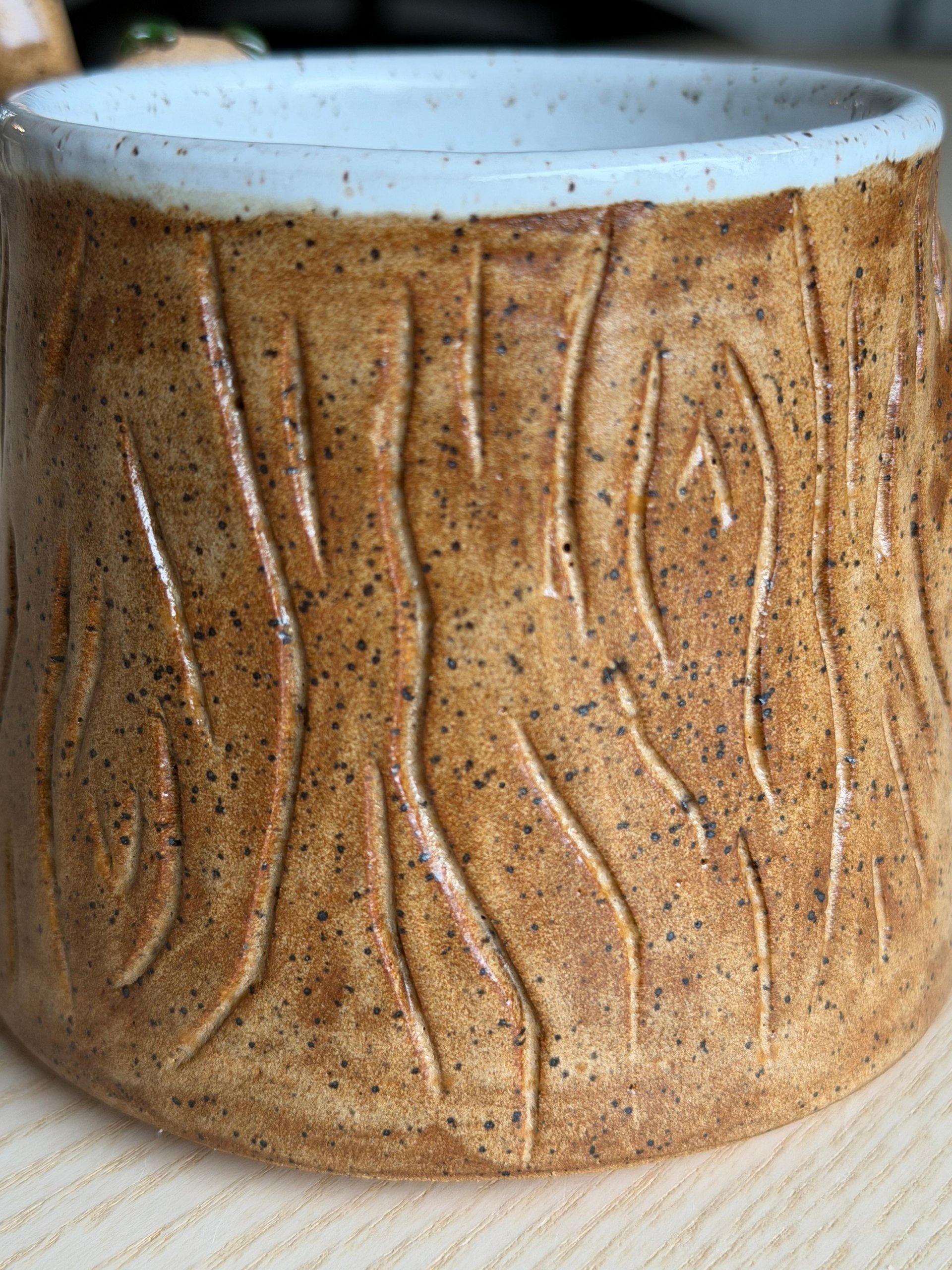 A honey-coloured mug with a white rim and deeply carved bark