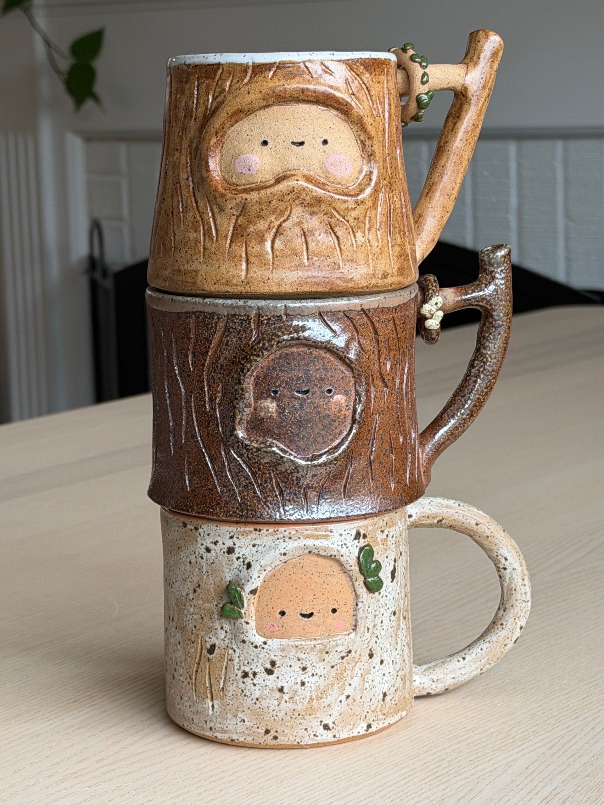 Three tree bark mugs stacked one on top of another, each with a sleepy face